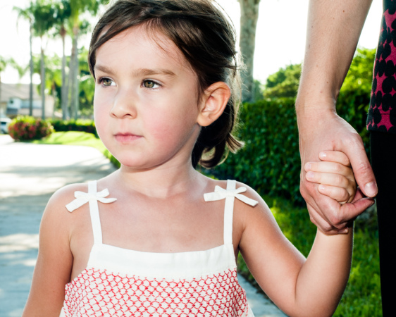 A young girl holding an adult's hand while walking outside.