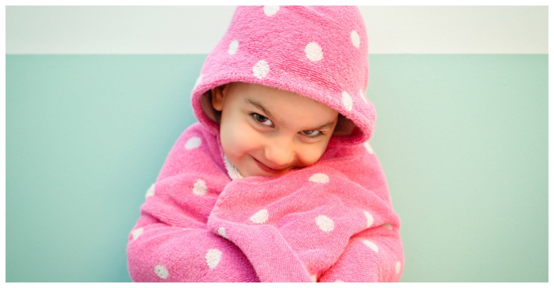 Child wrapped in a pink polka-dot towel, smiling logically at the camera.