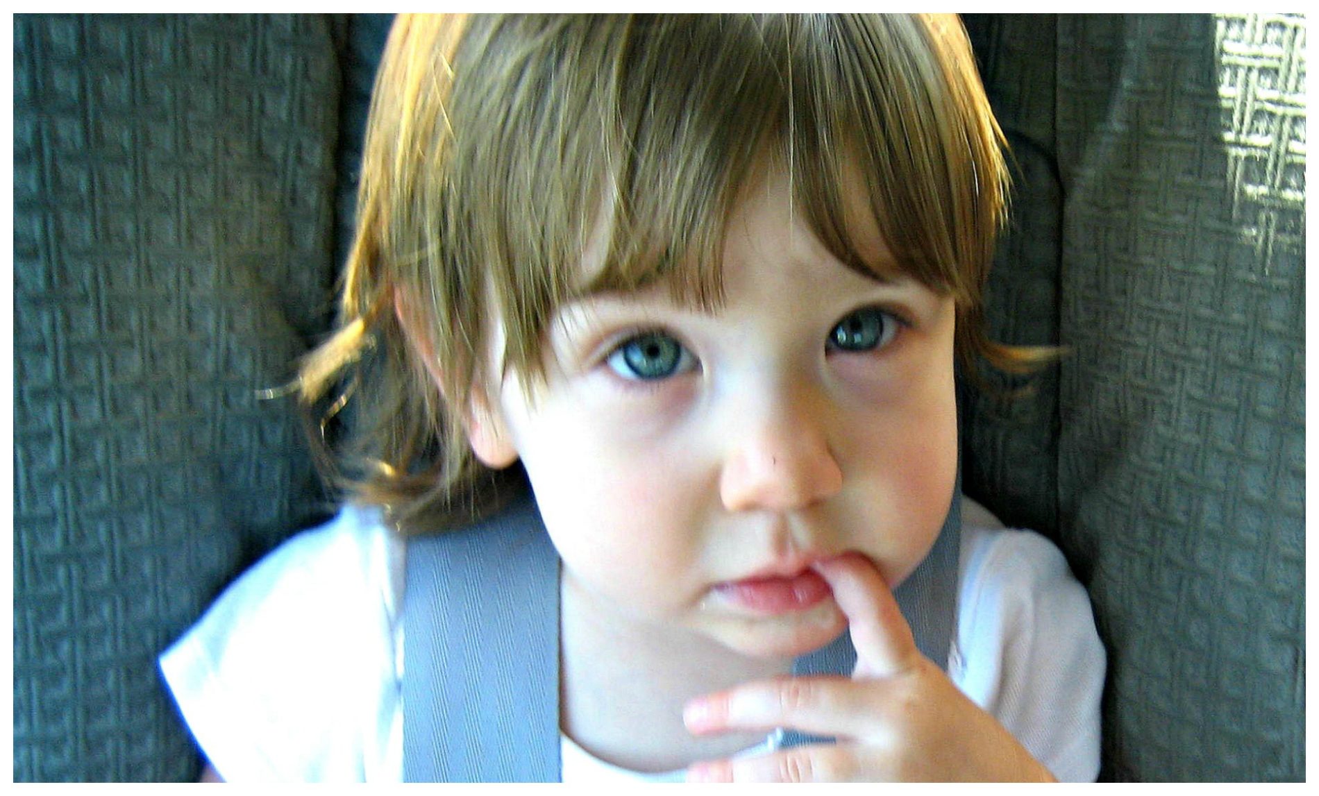 Young child with blue eyes and brown hair seated with finger on lips, displaying thoughtful behavior.