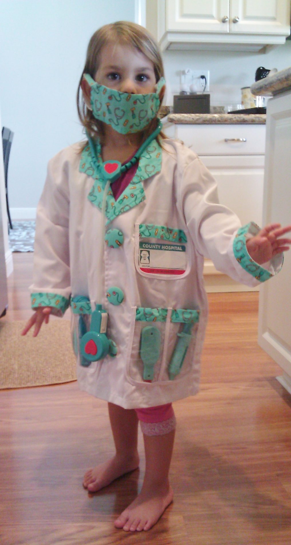 A child dressed in a lab coat with toy medical equipment is pretending to be a doctor, much as you might expect.
